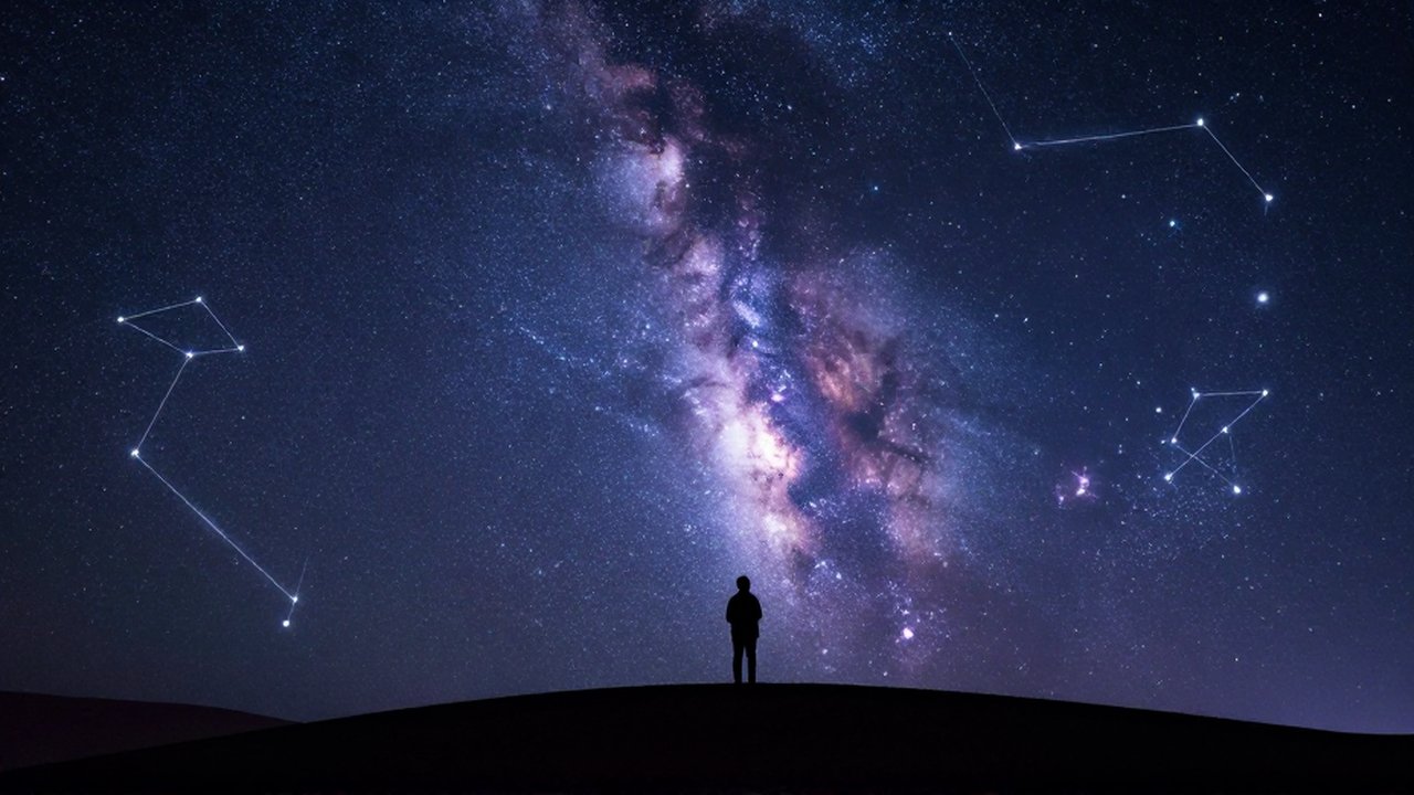 Silueta de una persona contemplando la Vía Láctea y constelaciones en un cielo nocturno estrellado.