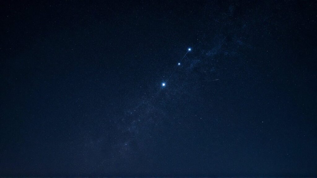 Tres estrellas brillantes del cinturón de Orión alineadas en un cielo nocturno profundo.