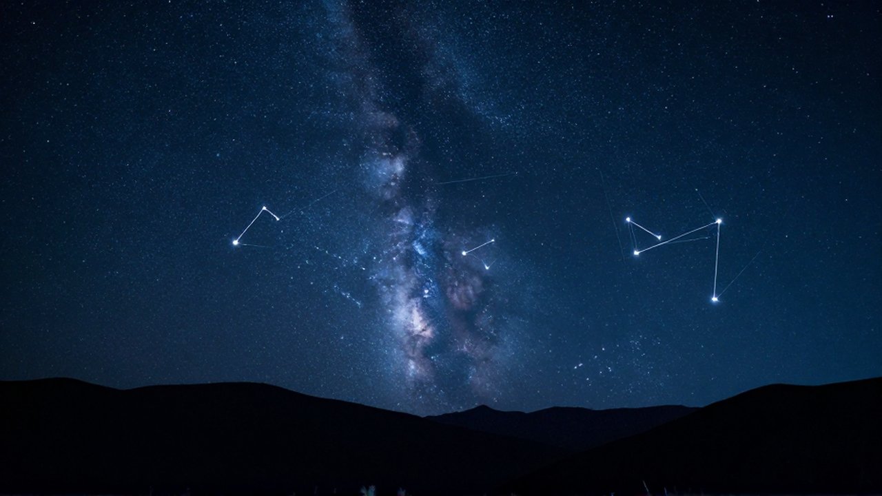 Cielo nocturno estrellado con constelaciones brillantes y la Vía Láctea sobre montañas tranquilas.