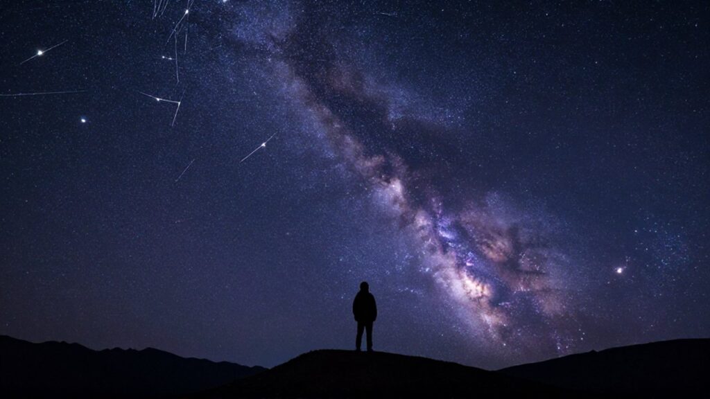 Silueta de un astrónomo contemplando un cielo nocturno estrellado y la Vía Láctea desde una montaña.