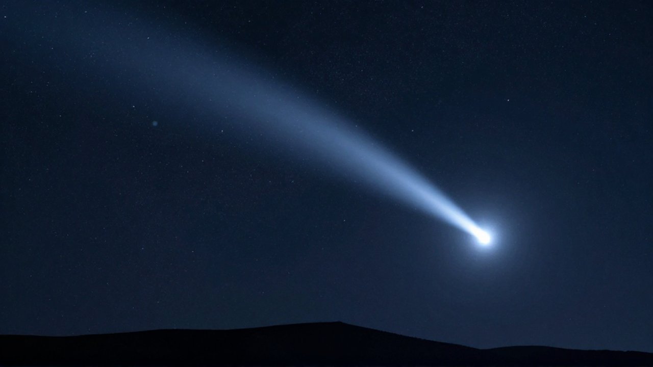 Cometa brillante de cola larga cruzando un cielo estrellado sobre la silueta de montañas.