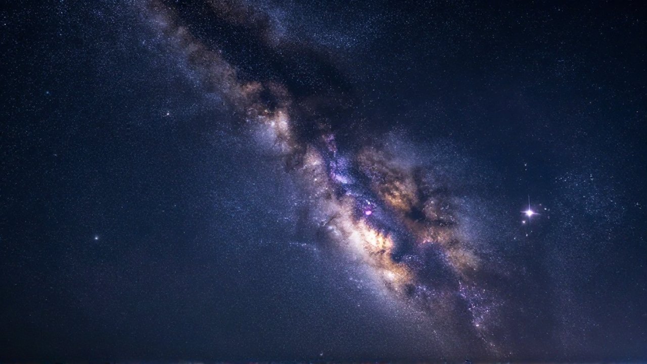 La Vía Láctea cruza el cielo nocturno iluminando cúmulos estelares y nebulosas en tonos violetas.