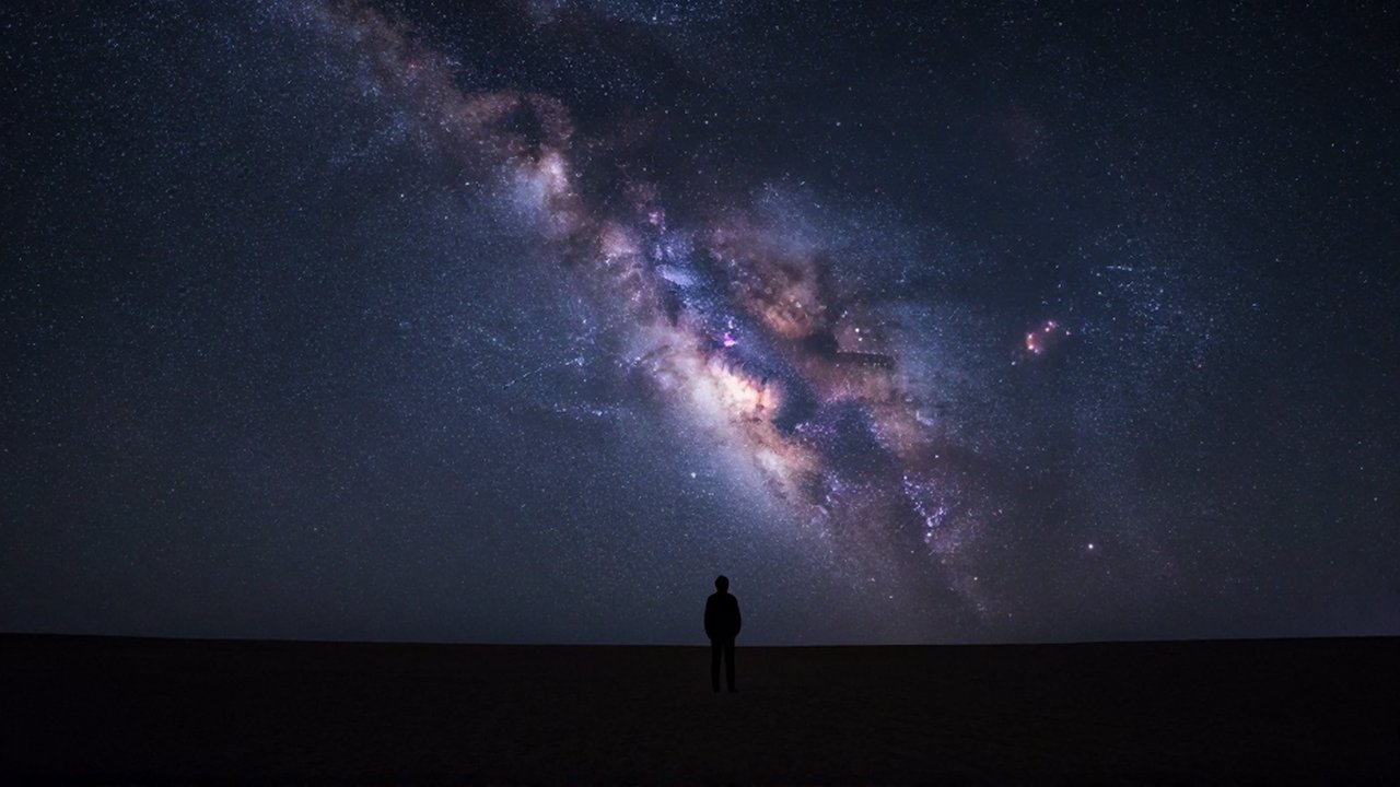 Silueta de un astrónomo contemplando la inmensidad de la Vía Láctea en un desierto nocturno.