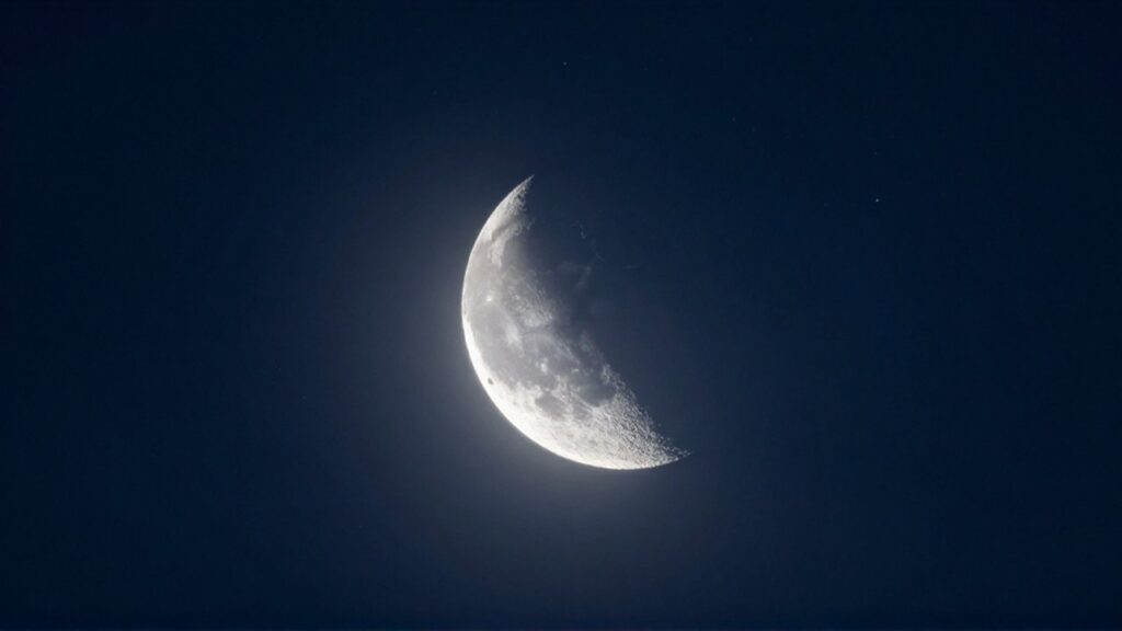 Luna creciente brillante sobre un cielo nocturno azul profundo con estrellas y nubes tenues.